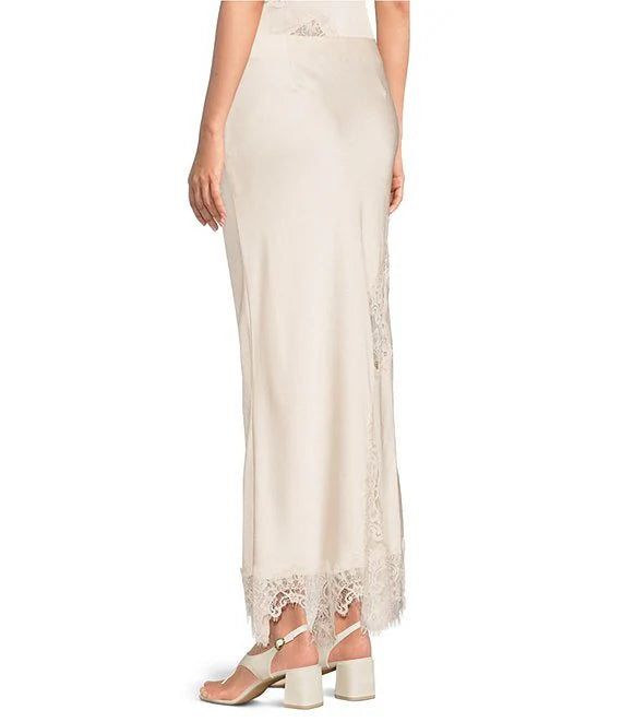 A model wearing a floor-length cream satin skirt with sheer lace side panels and a matching lace hem, paired with beige block-heel sandals against a white background.