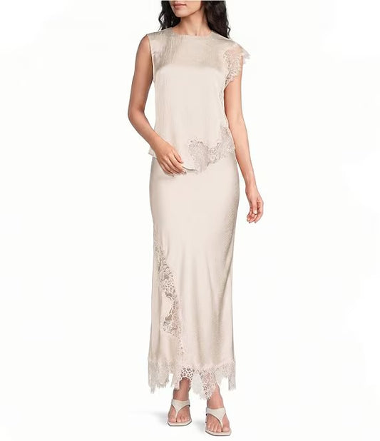 A woman modeling a sleeveless, floor-length champagne beige dress with sheer mesh cap sleeves and delicate lace trim details, paired with white strappy sandals against a plain white background.