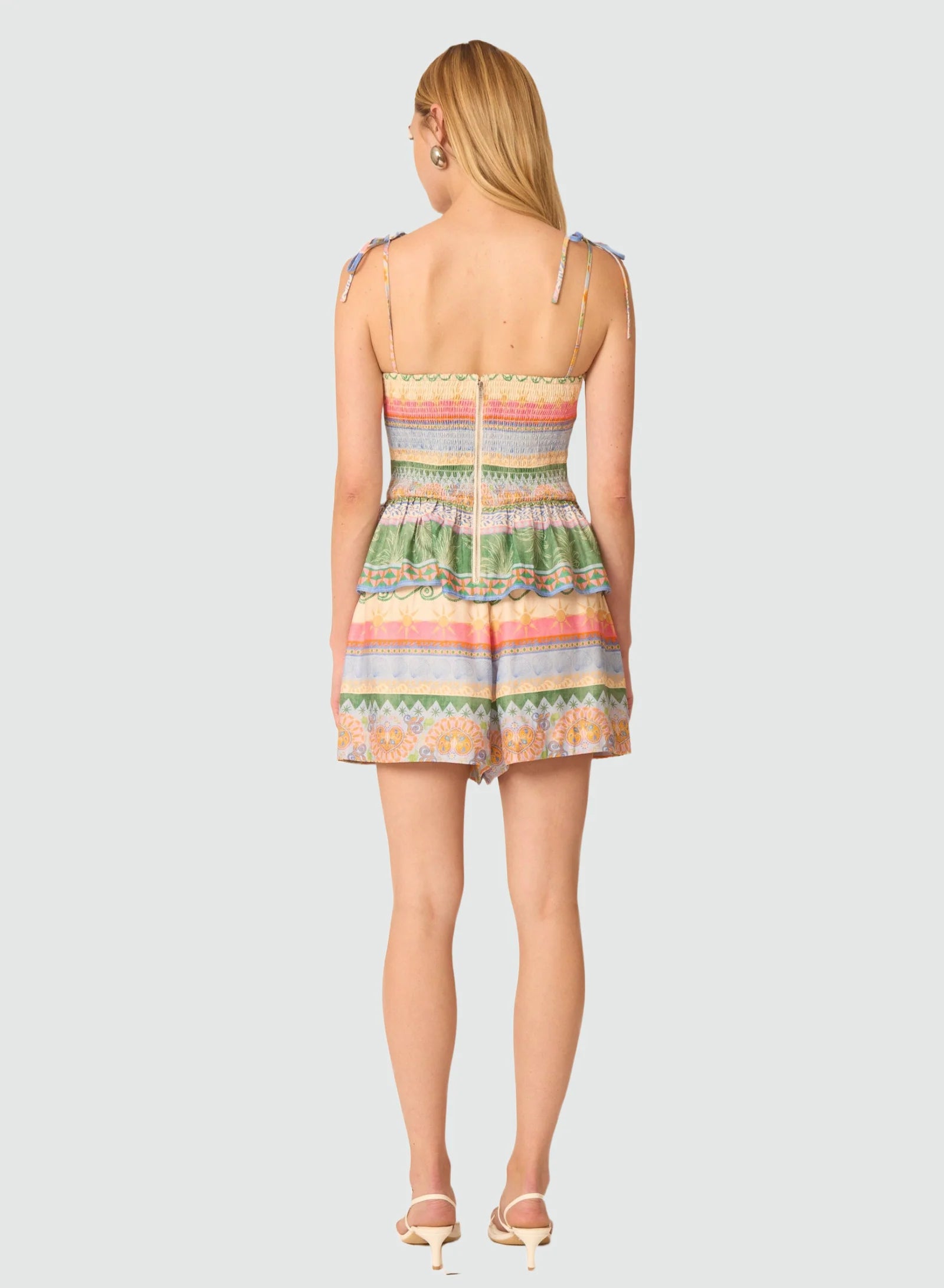 A woman shown from the back wearing a sleeveless mini dress with thin shoulder straps and a colorful horizontal striped pattern, photographed against a light gray studio background.