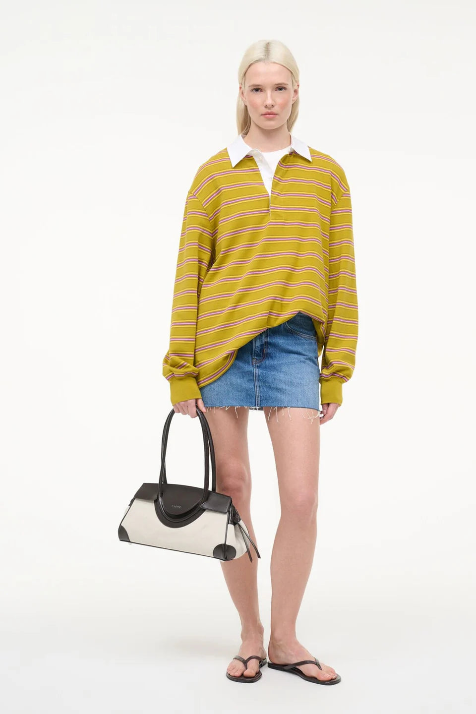 Woman wearing a yellow striped sweater and denim shorts, holding a black and white handbag on a white background