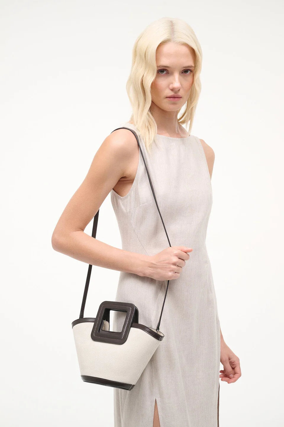 Woman holding a white handbag with a black bottom section on a white background