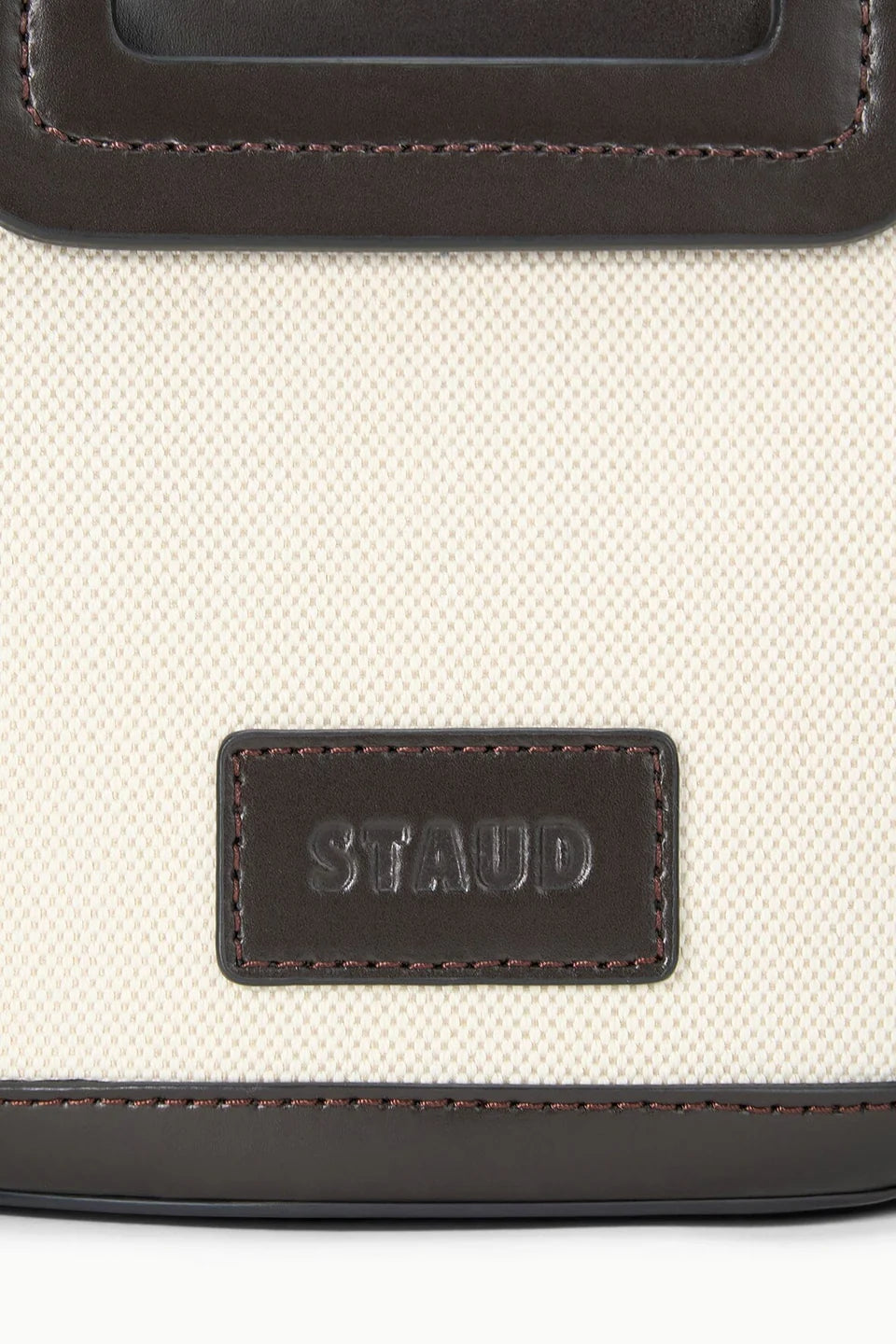 Close-up of a beige bag with brown leather trim and 'STAUD' logo.