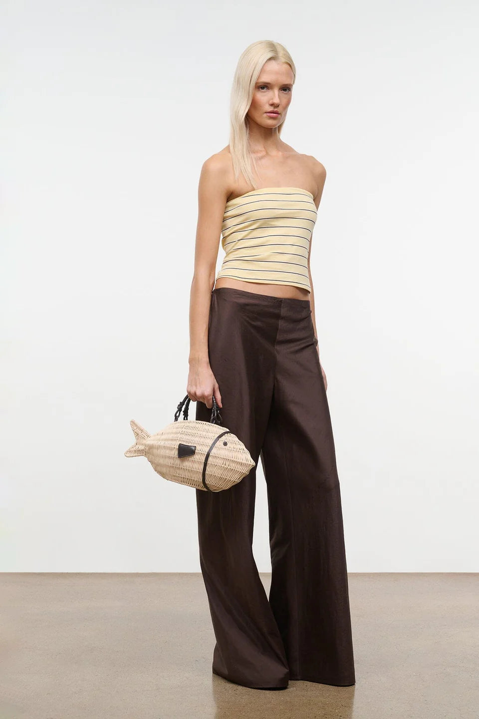 Woman wearing a strapless top and wide-leg pants holding a fish-shaped handbag against a white background