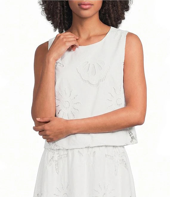 Woman wearing a white sleeveless top with lace details on a plain background