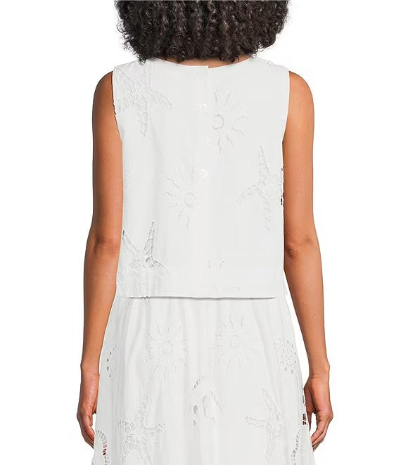 A sleeveless white eyelet dress shown from the back on a model, featuring embroidered floral details and a buttoned neckline.