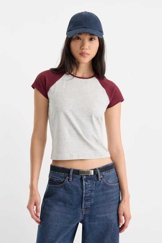 Person wearing a gray and red baseball shirt with blue jeans and a navy cap on a white background