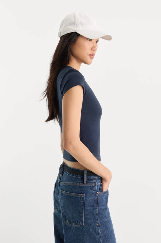 Woman wearing a navy sleeveless top and blue jeans with a beige cap on a white background