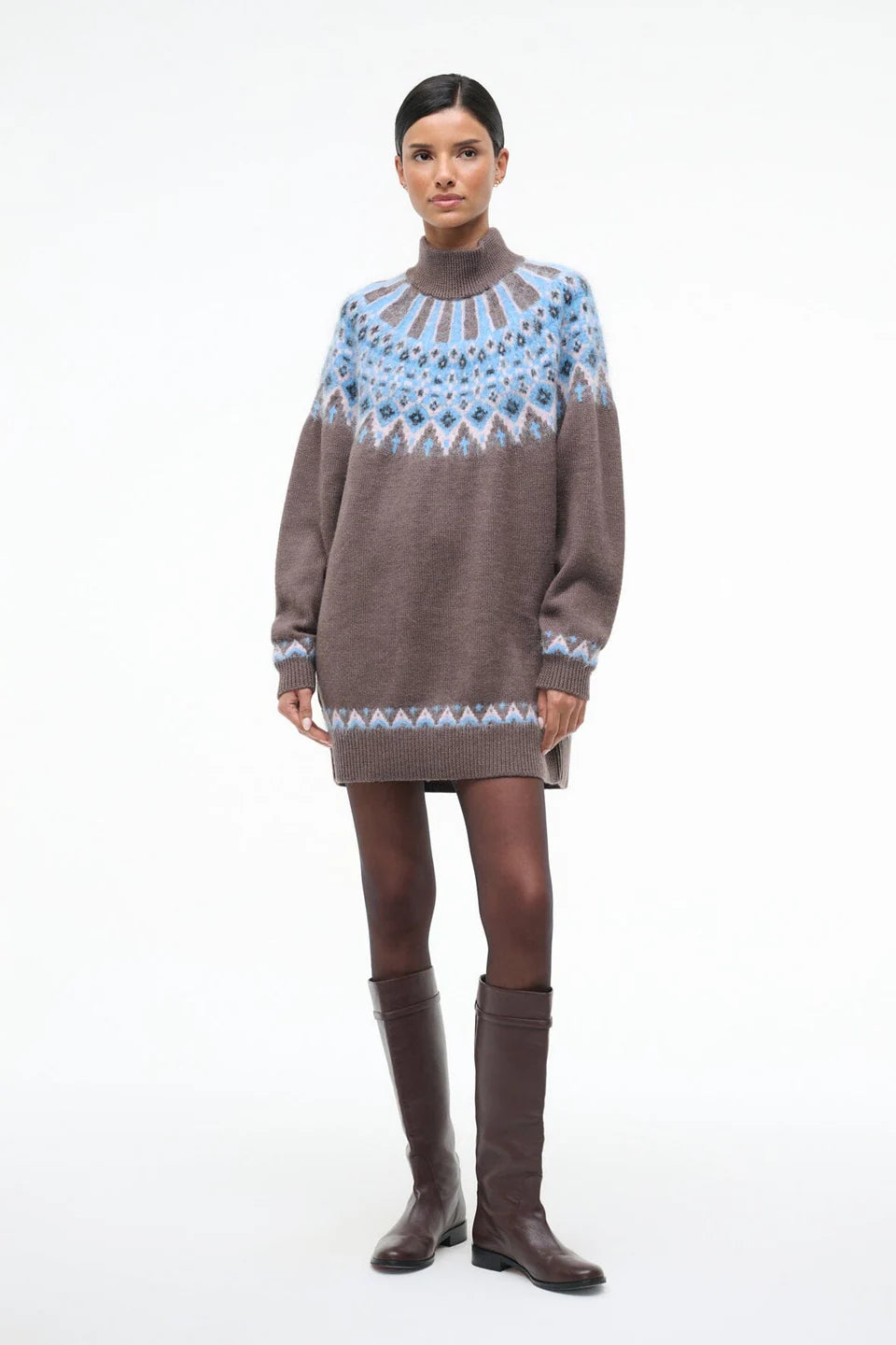 Woman wearing a brown sweater dress with a blue and white pattern and brown knee-high boots on a white background