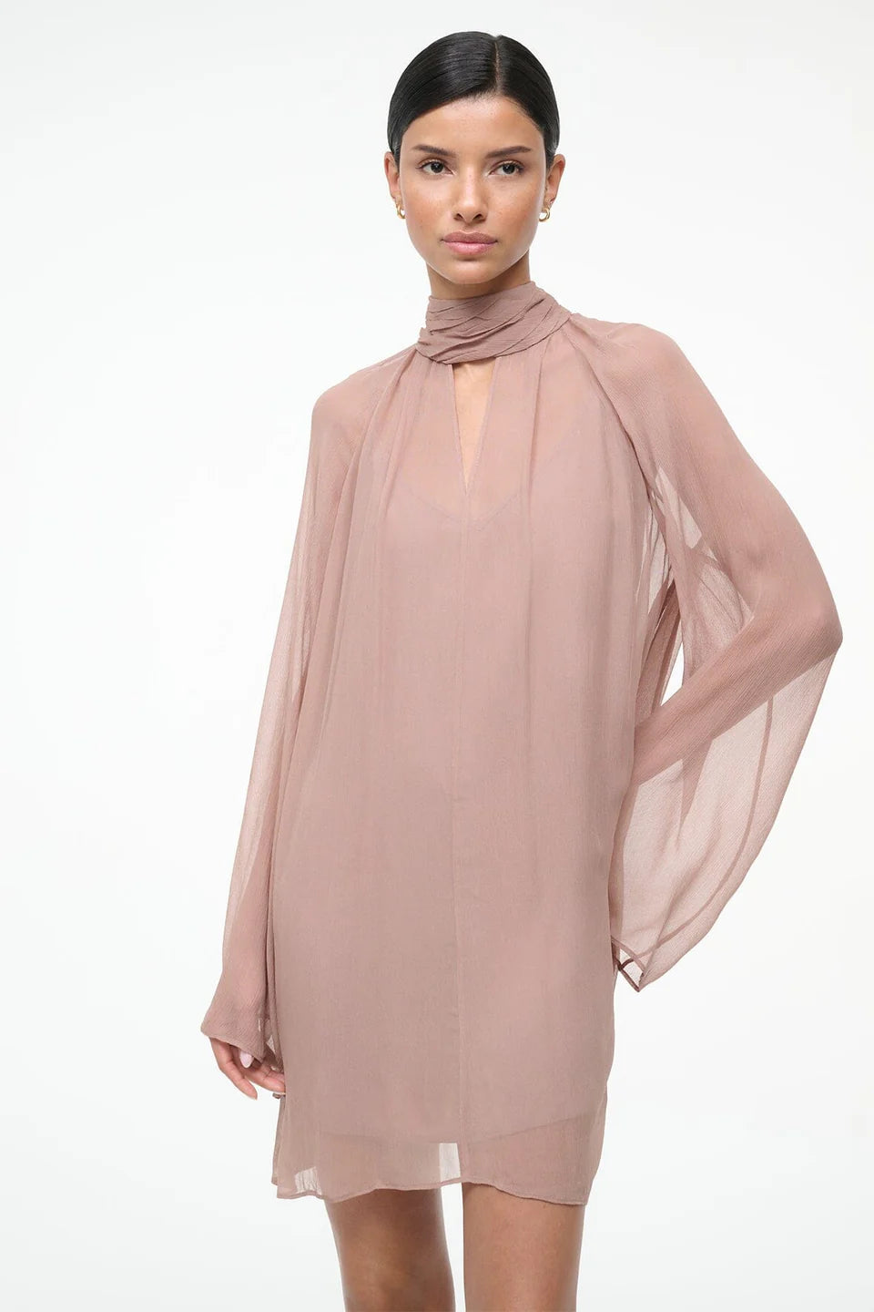 Woman wearing a light pink dress with a sheer overlay on a white background
