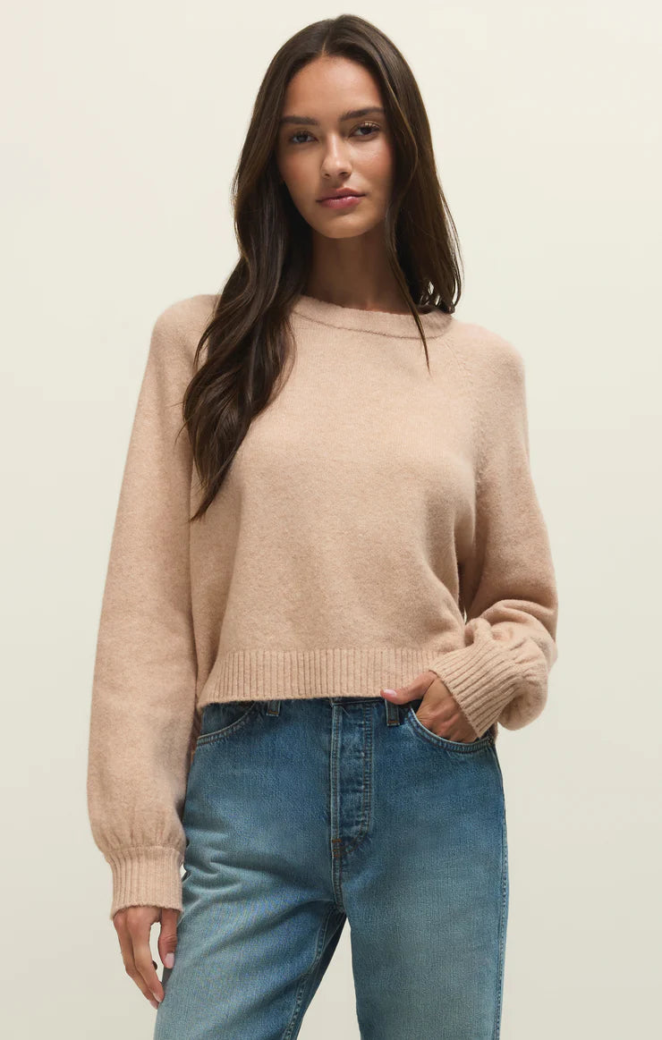 Woman wearing a beige sweater and blue jeans against a plain background