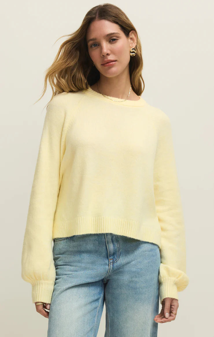 Woman wearing a light yellow sweater and blue jeans against a plain background