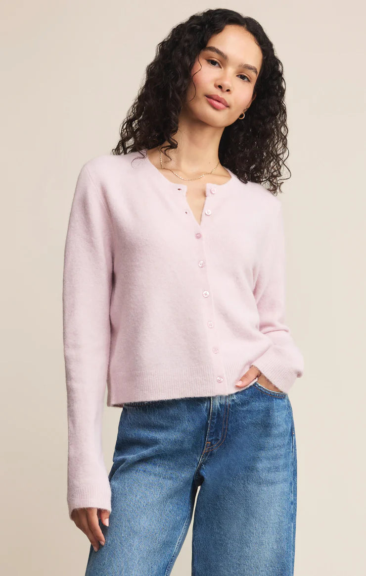 Woman wearing a light pink button-up shirt and blue jeans against a beige background