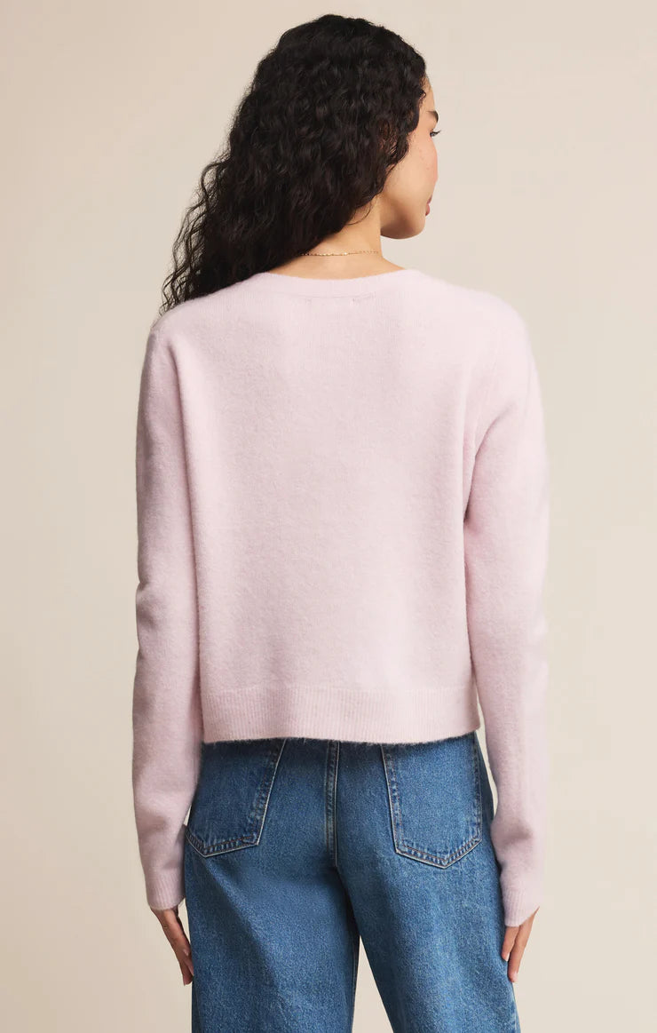 Person wearing a light pink sweater and blue jeans against a beige background