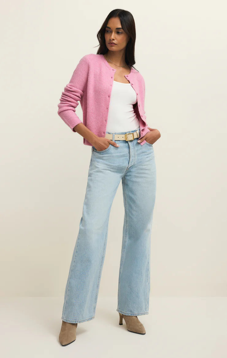 Woman wearing a pink cardigan, white top, light blue jeans, and beige shoes on a plain background