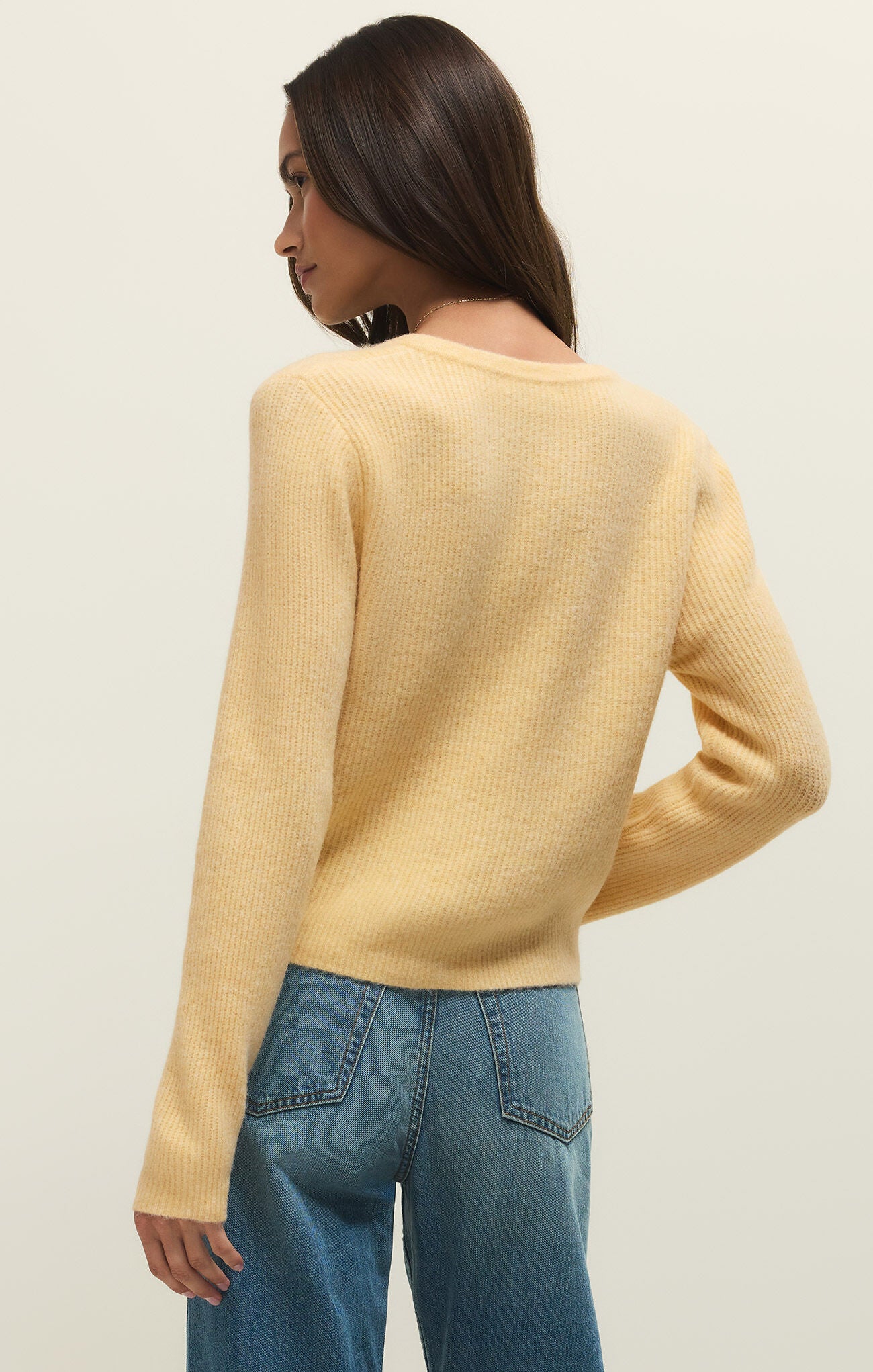 Woman wearing a yellow sweater and blue jeans against a plain background