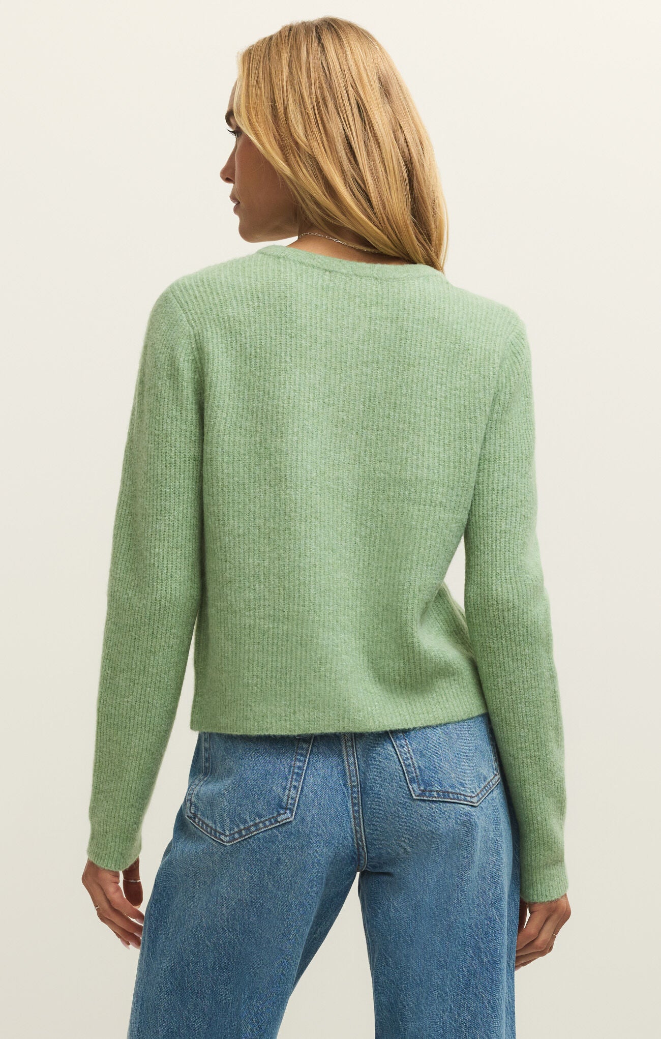 Person wearing a green sweater and blue jeans on a plain background