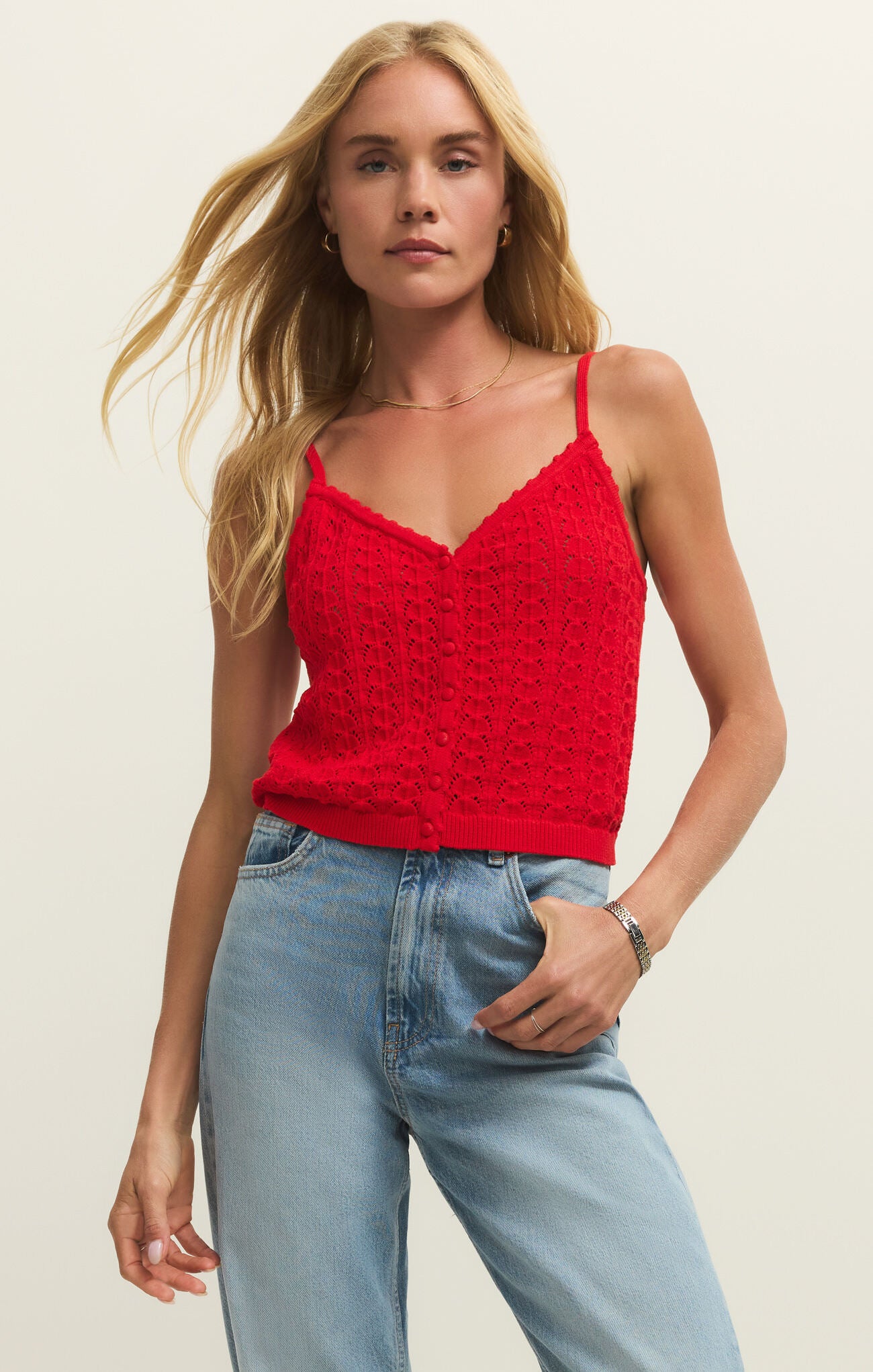 Woman wearing a red knitted tank top and light blue jeans on a plain background