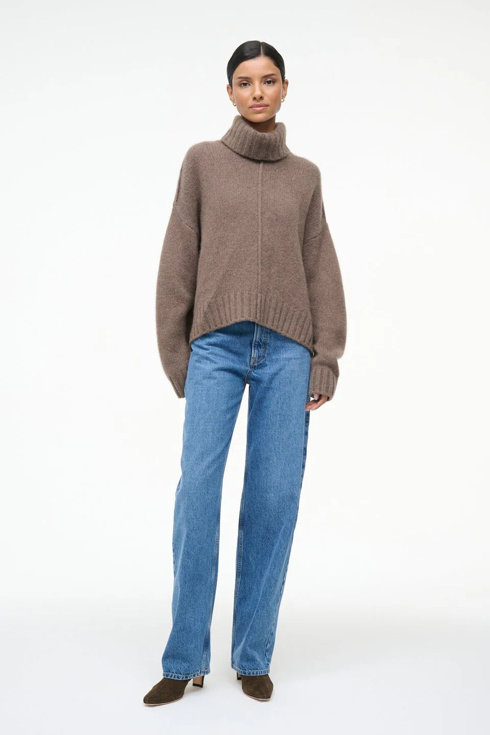 Person wearing a brown turtleneck sweater and blue jeans on a white background