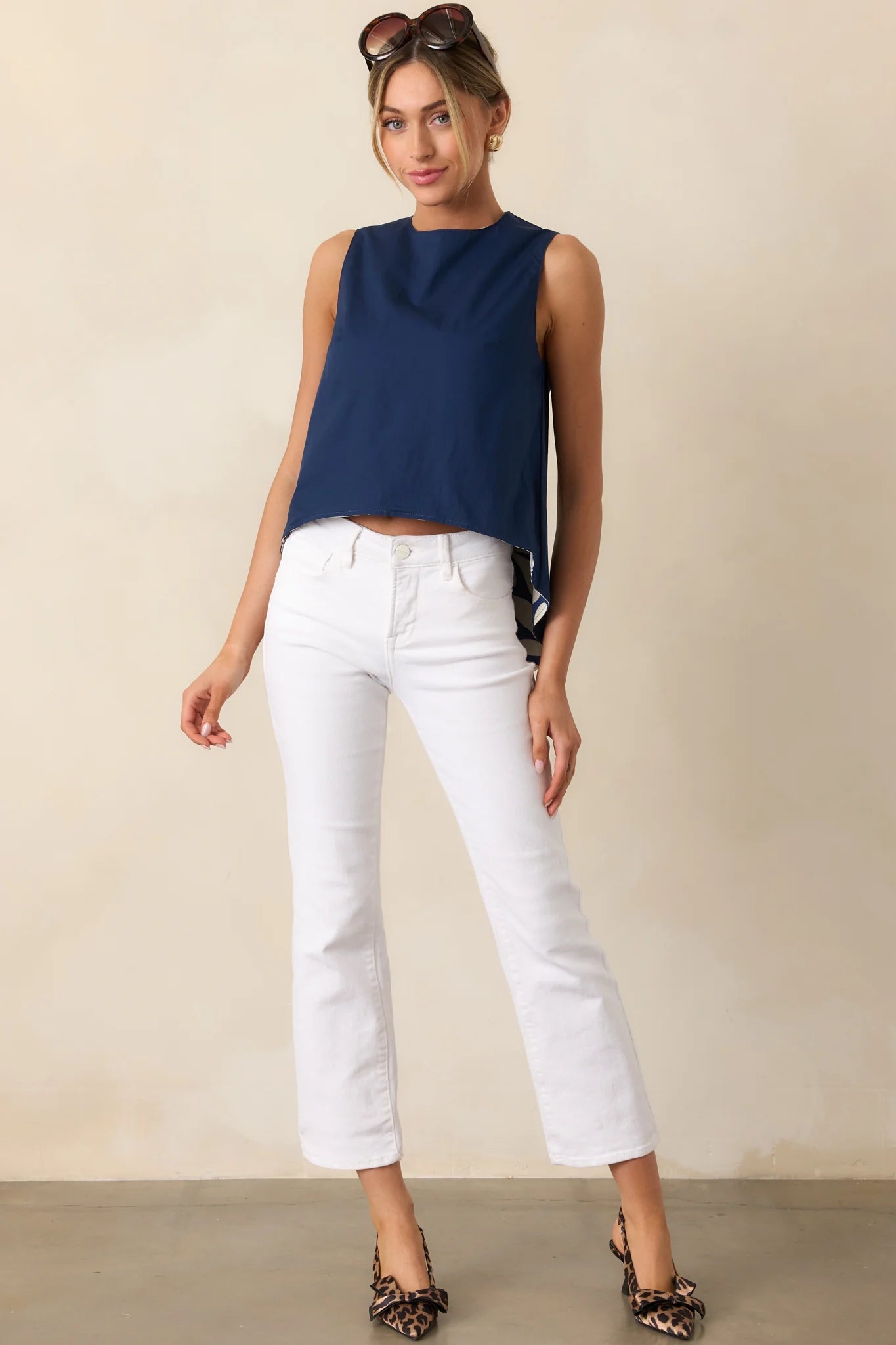 Woman wearing a navy sleeveless top and white pants against a beige background