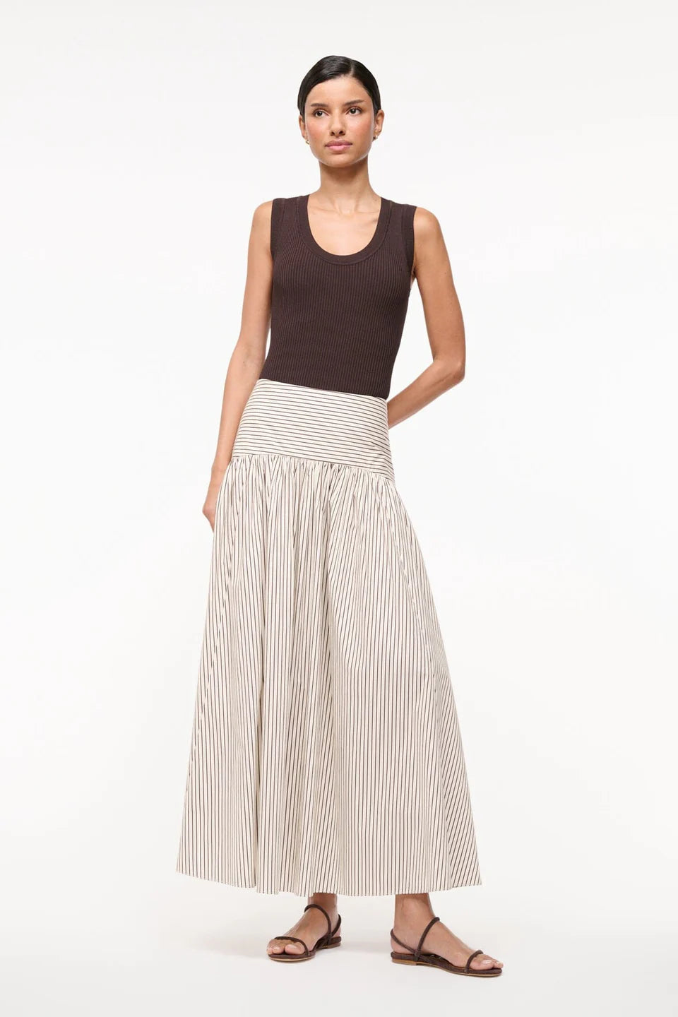 Woman wearing a brown sleeveless top and beige pleated skirt on a white background
