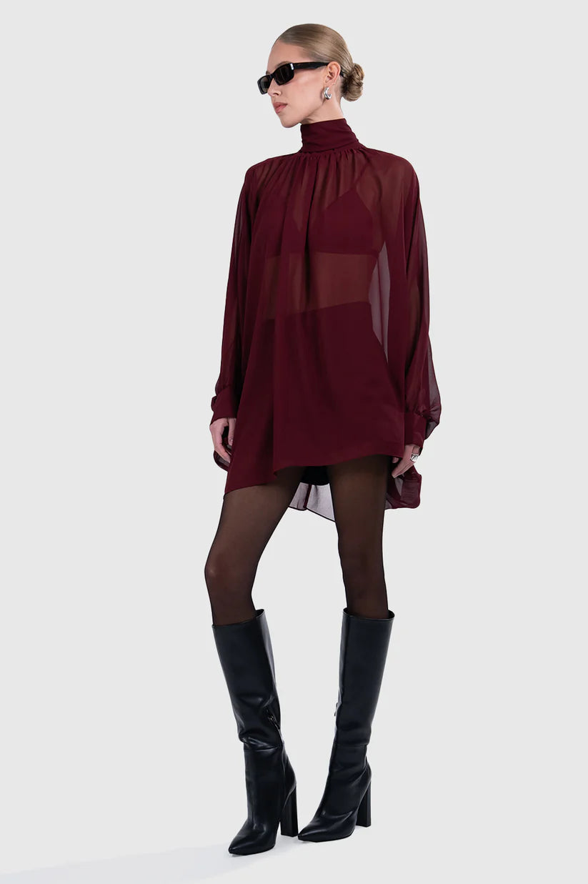Woman wearing a burgundy long-sleeve top and black knee-high boots on a white background