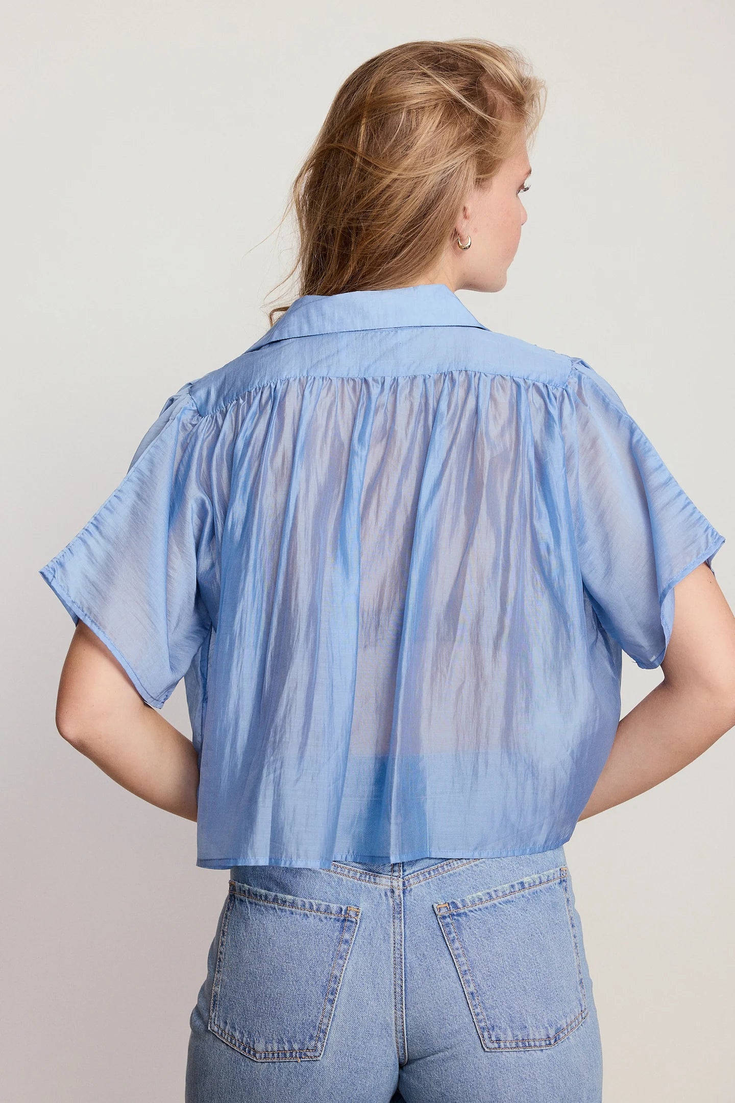 Woman wearing a sheer blue blouse over a denim shirt against a plain background