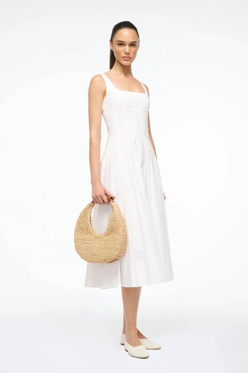Woman in a white dress holding a woven bag on a white background