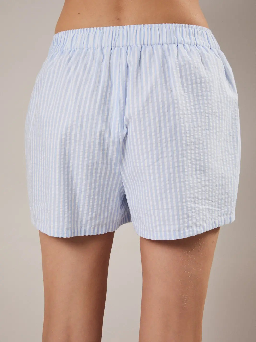 Light blue striped shorts worn by a person on a beige background