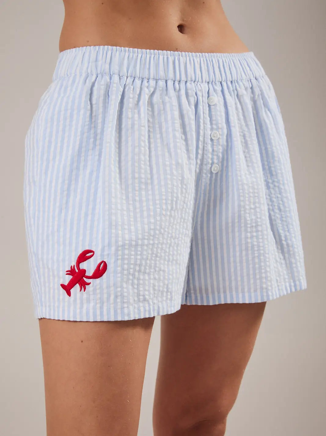 Light blue striped shorts with a red lobster design on a neutral background