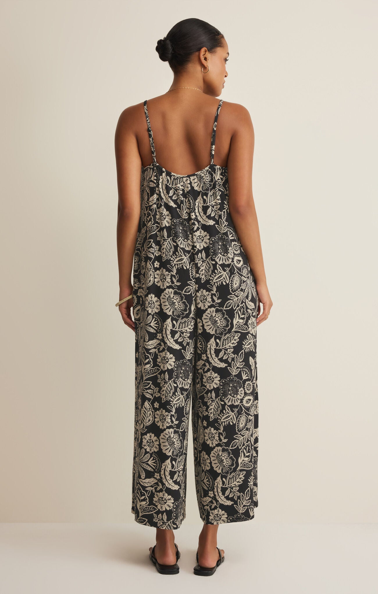 Woman wearing a black and white floral jumpsuit on a beige background