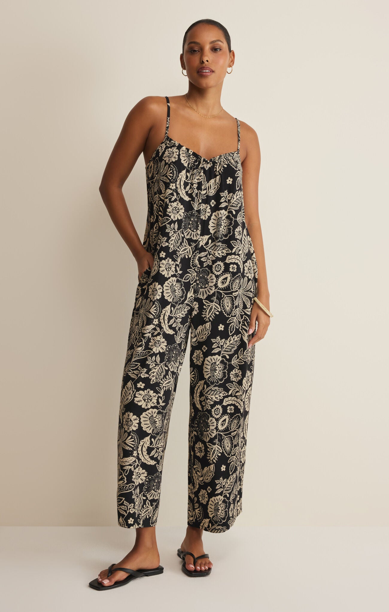 Woman wearing a black and white floral jumpsuit on a beige background