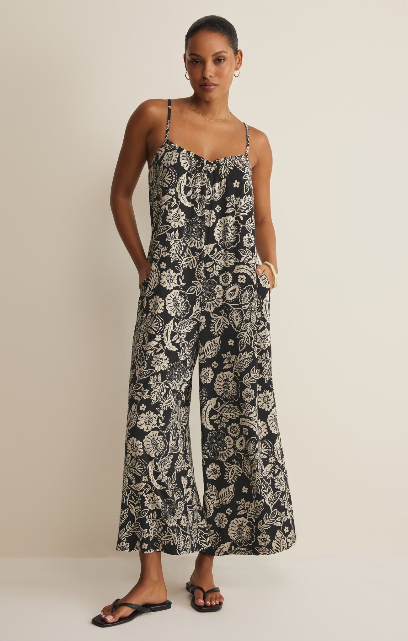 Woman wearing a black and white floral patterned jumpsuit on a beige background