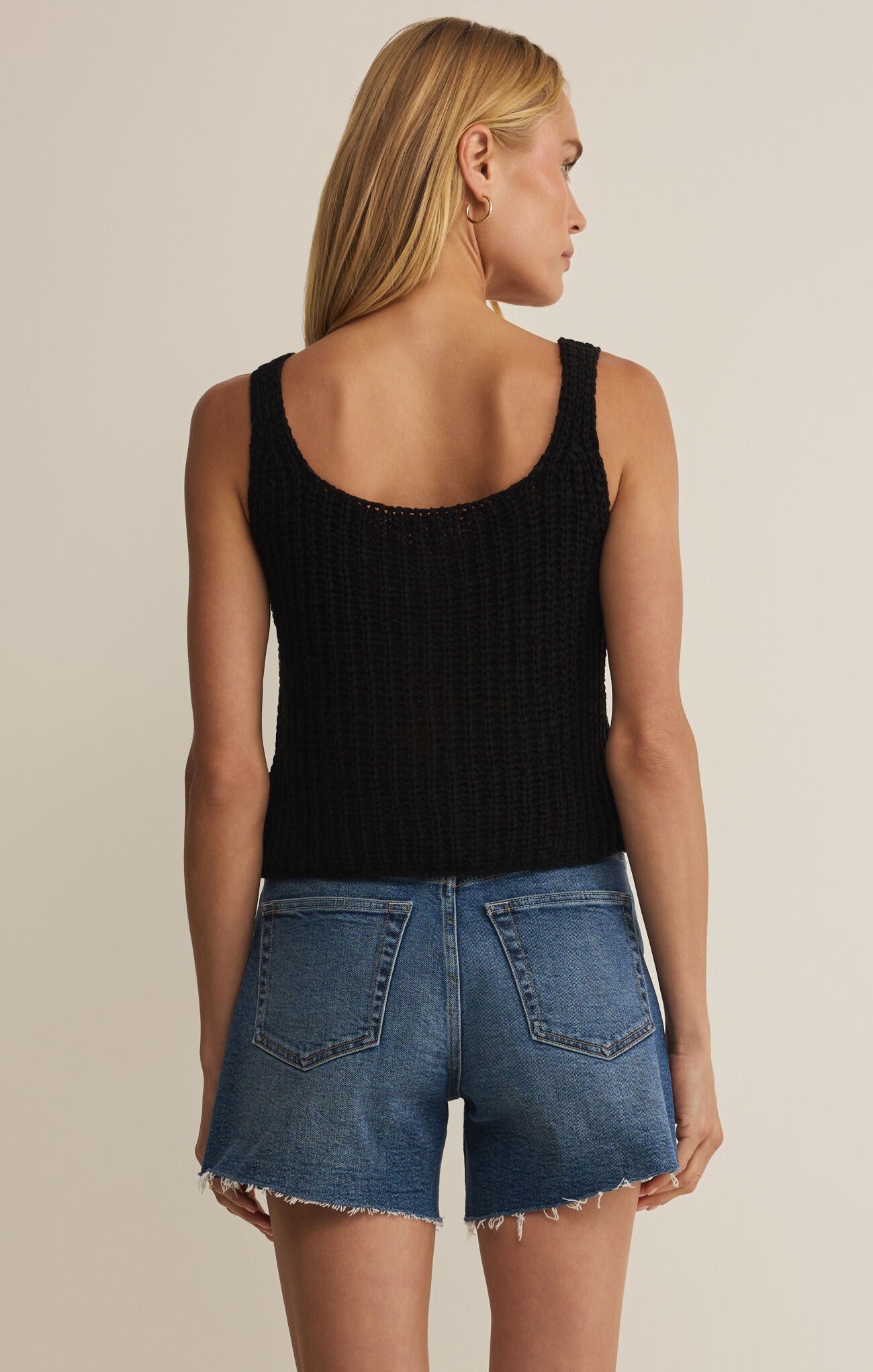 Woman wearing a black tank top and blue denim shorts on a beige background