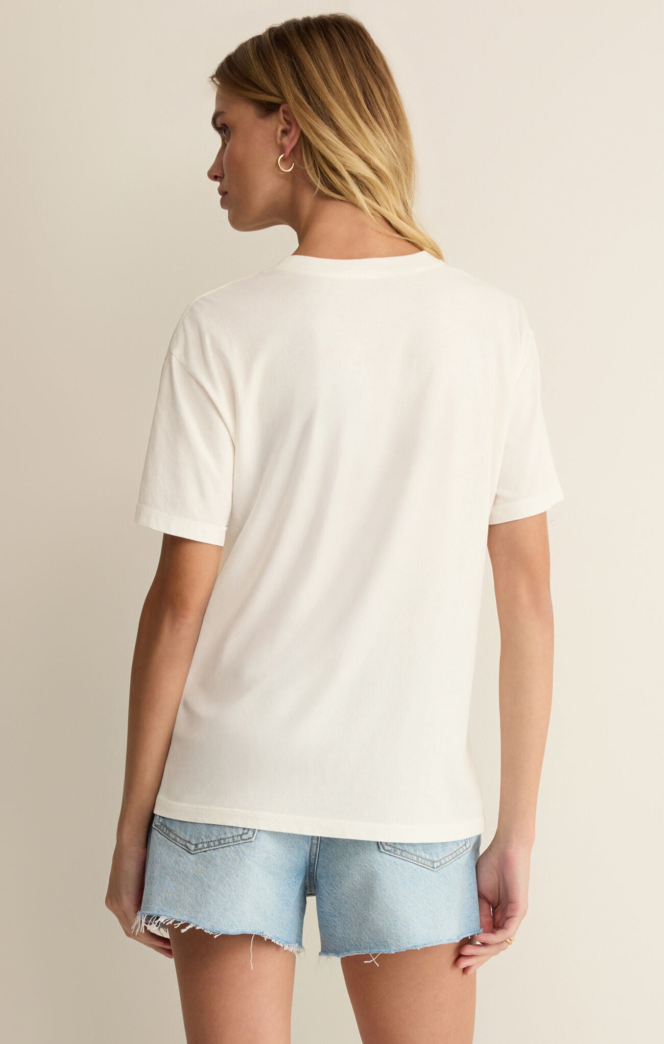 Woman wearing a plain white t-shirt and light blue denim shorts on a neutral background
