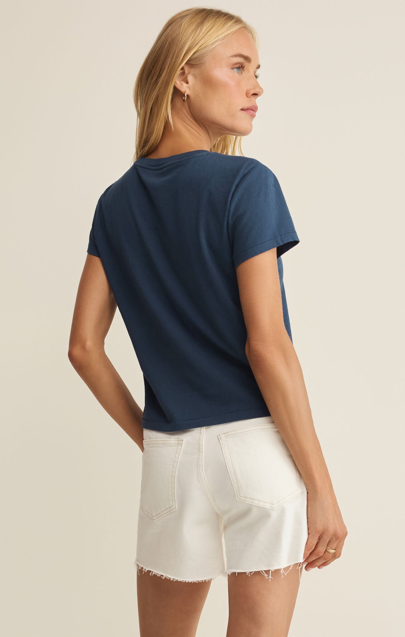 Woman wearing a navy blue t-shirt and white shorts on a beige background