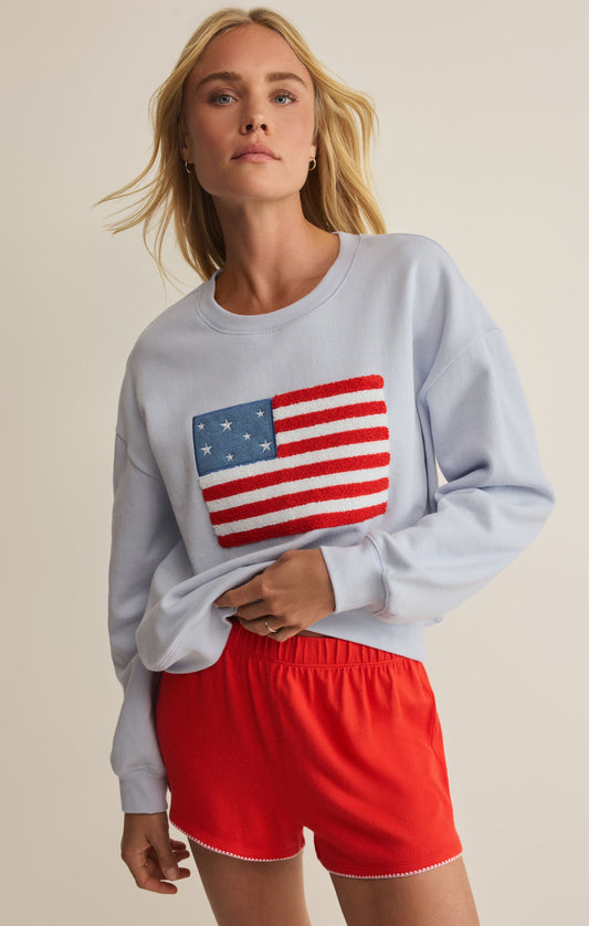 Woman wearing a light blue sweatshirt with an American flag design and red shorts on a beige background