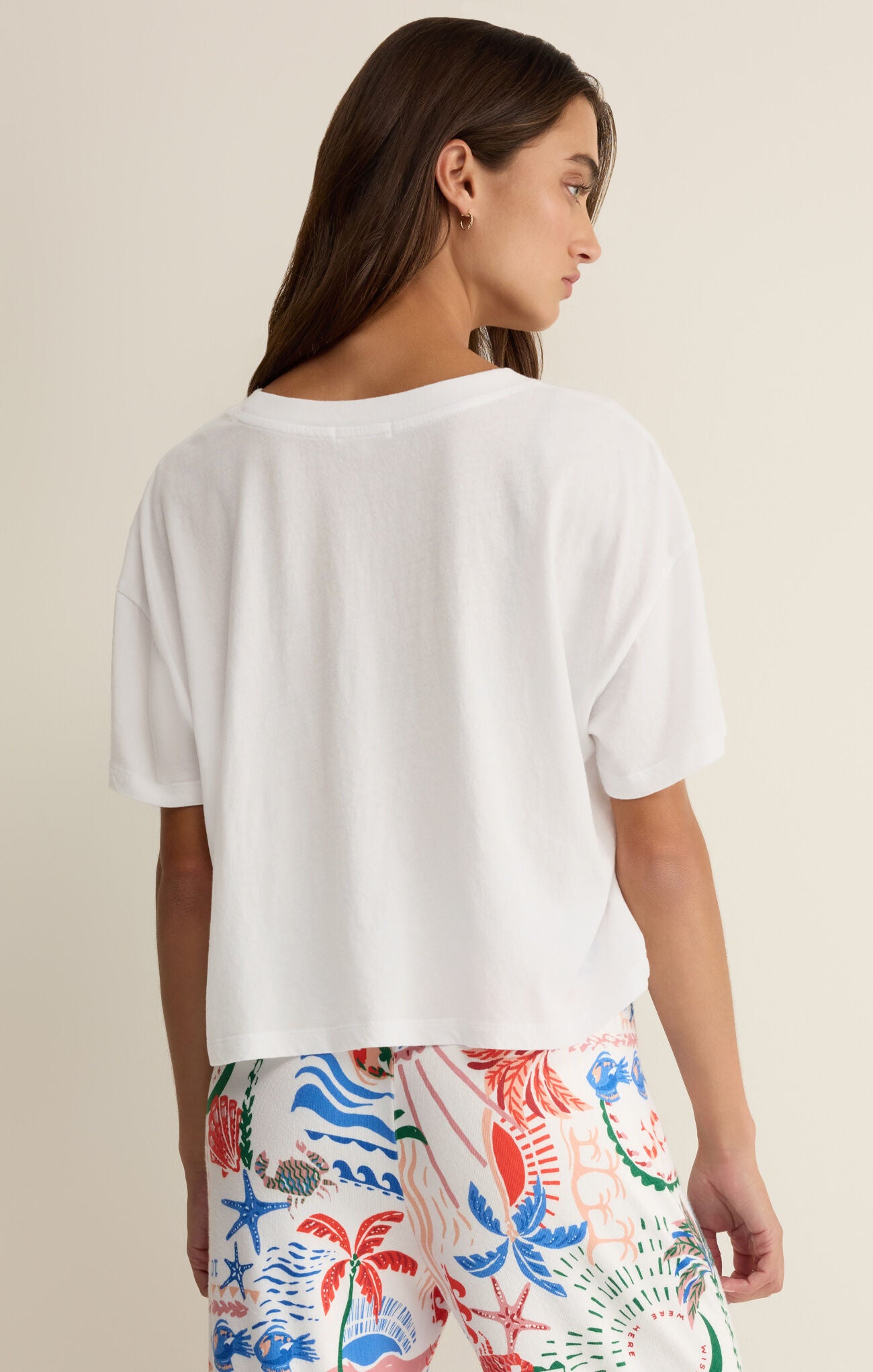 Woman wearing a white t-shirt and colorful floral pants on a beige background