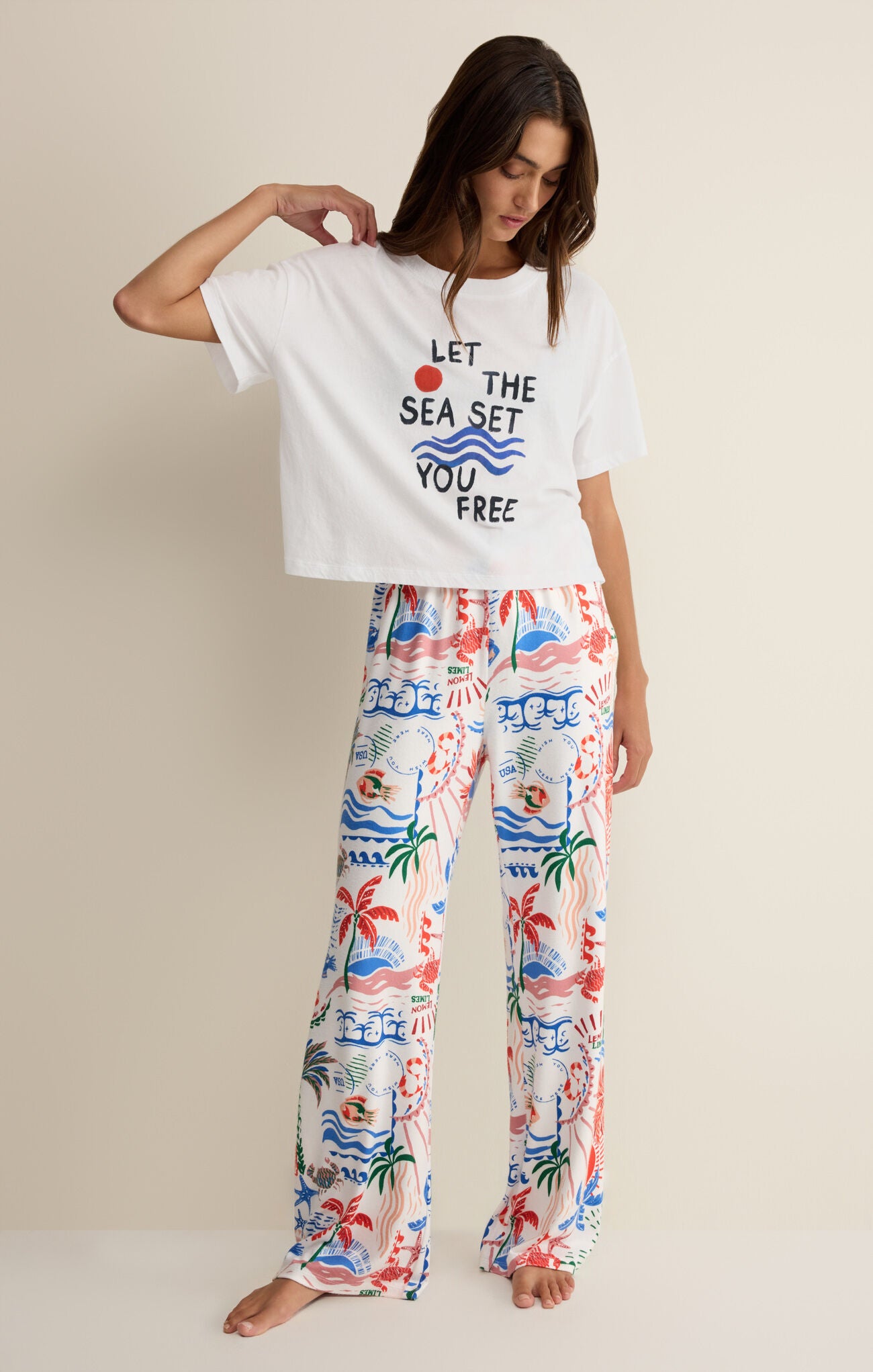 Woman wearing a white t-shirt with text and colorful pants on a beige background