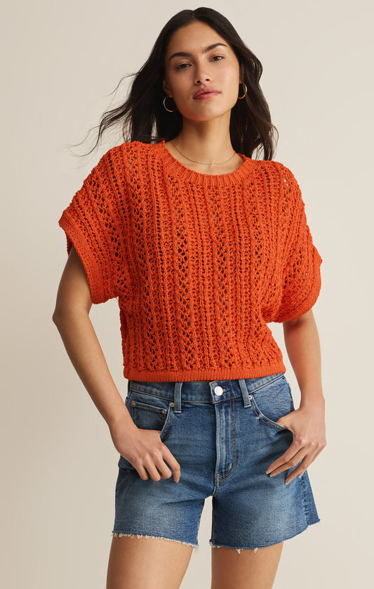 Woman wearing an orange knitted top and denim shorts on a beige background