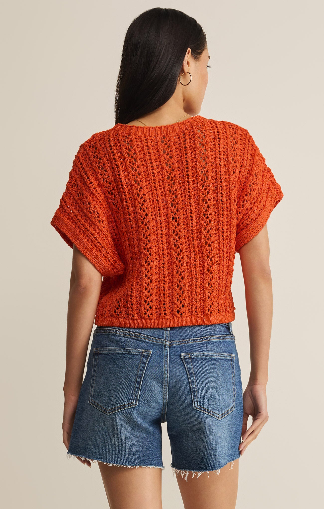 Person wearing an orange knitted top and denim shorts on a beige background