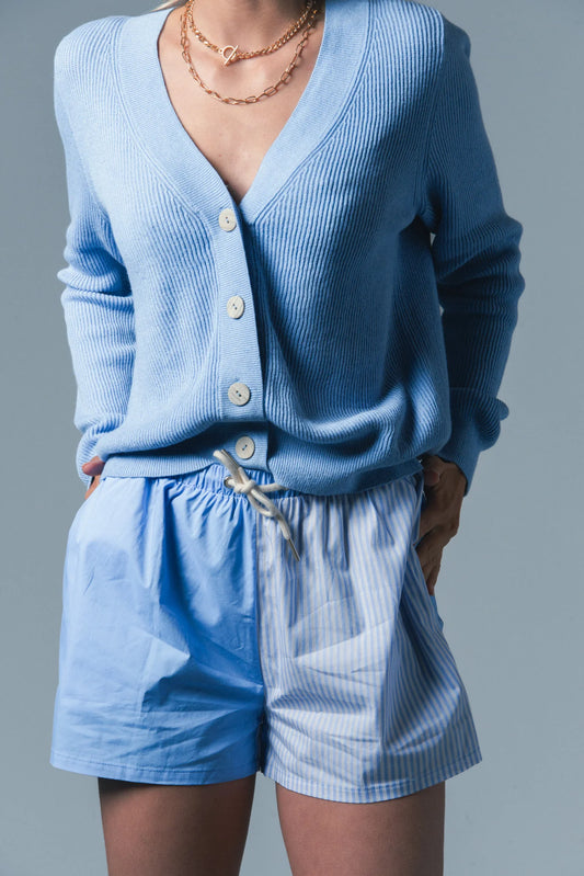 Person wearing a blue cardigan and shorts set against a gray background