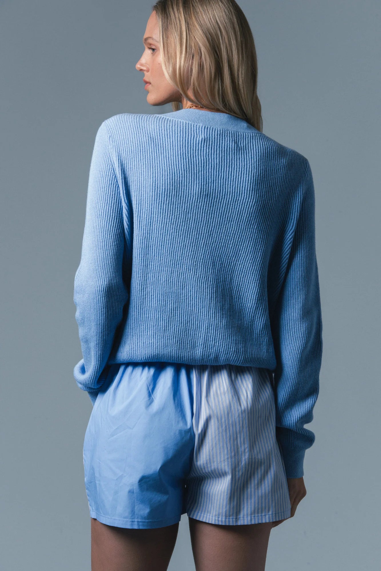 Woman wearing a blue ribbed sweater and shorts set against a gray background
