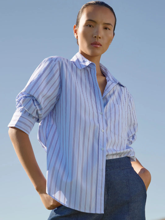 Person wearing a light blue and white striped shirt with rolled-up sleeves against a clear sky.