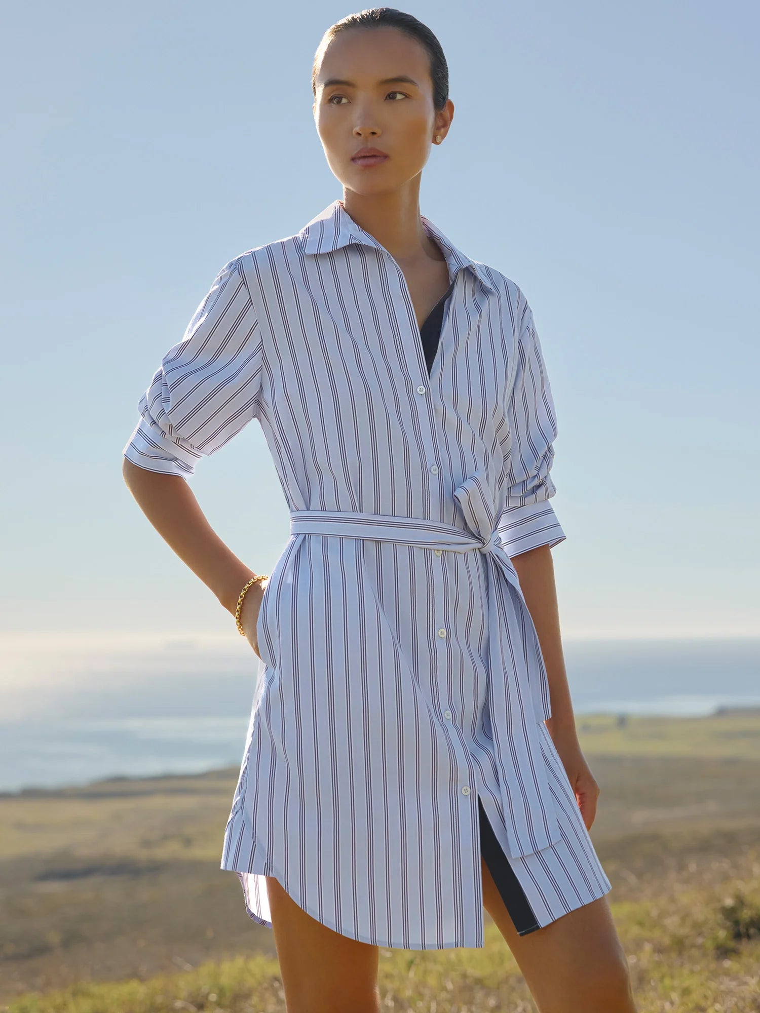 Woman wearing a striped shirt dress standing outdoors with a scenic background