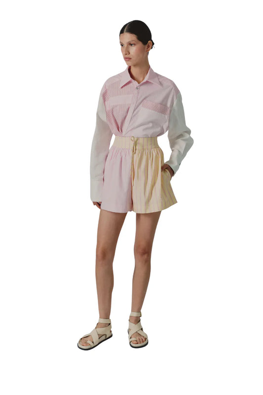 Woman wearing a light pink shirt and beige shorts on a white background