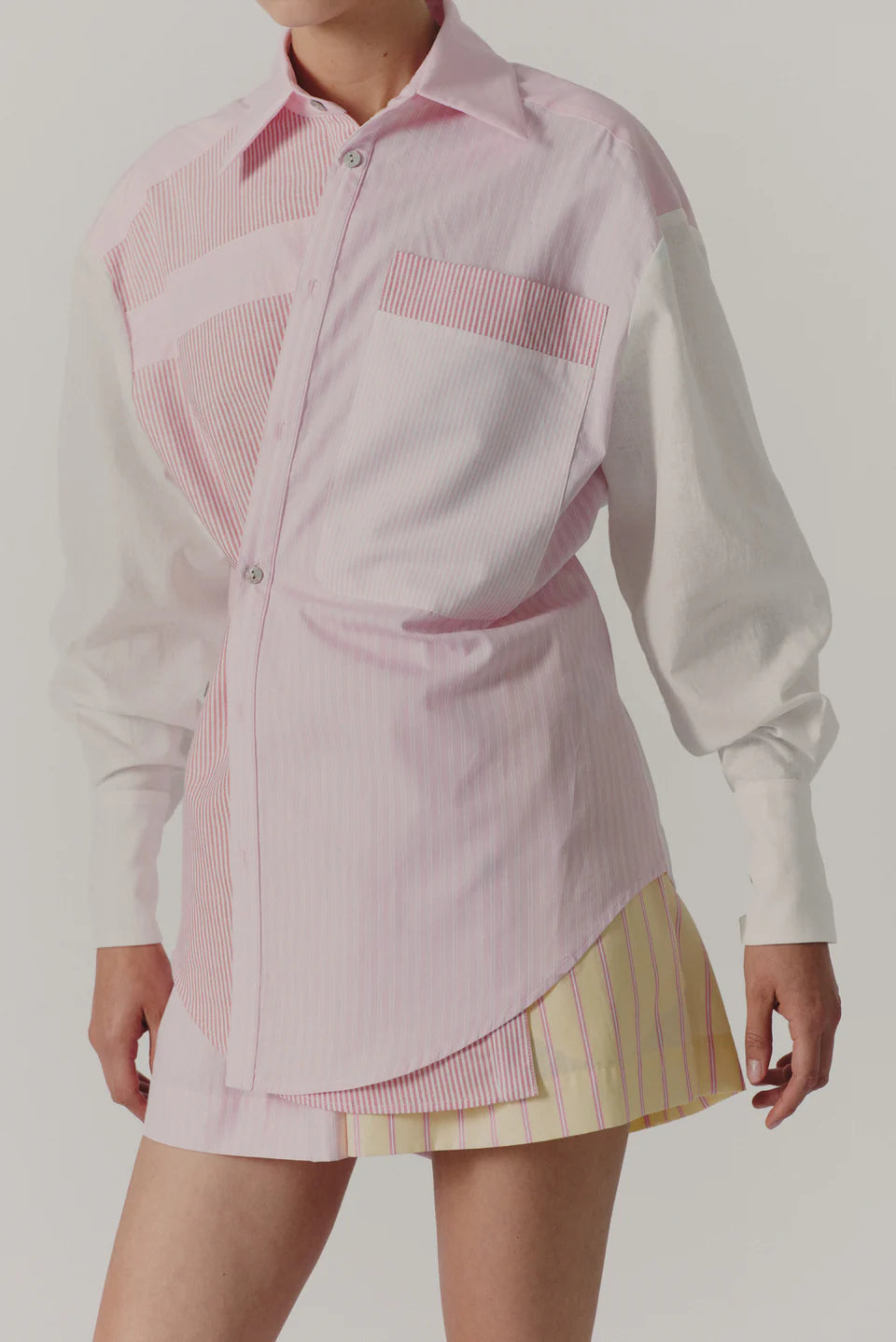 Person wearing a pink and white checkered shirt with a skirt on a plain background