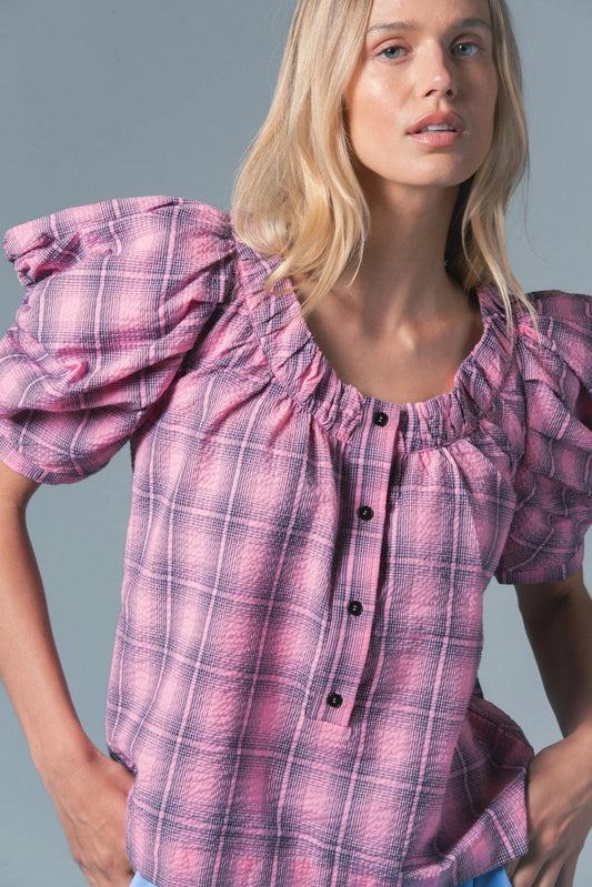 Woman wearing a pink plaid blouse against a gray background
