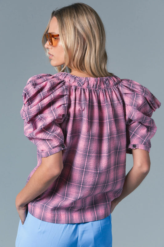 Woman wearing a pink plaid blouse with ruffled sleeves on a gray background