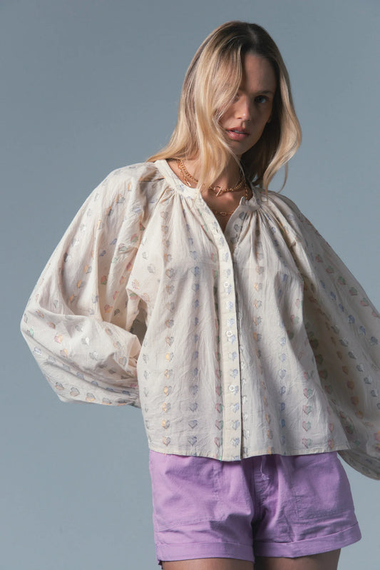 Woman wearing a light blouse with puffed sleeves and purple shorts against a gray background