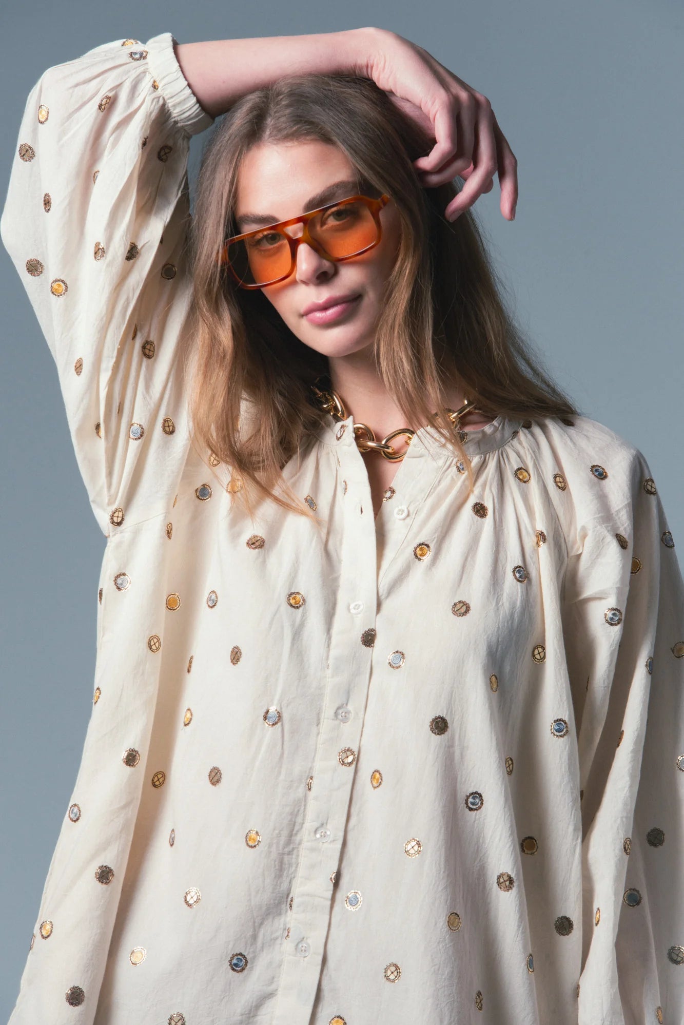 Woman wearing a cream-colored blouse with gold buttons against a gray background